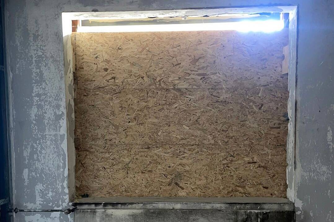 Entkerntes Zimmer mit rußgeschwärzten Betonwänden, das Fenster ist mit einer Holzplatte verschlossen