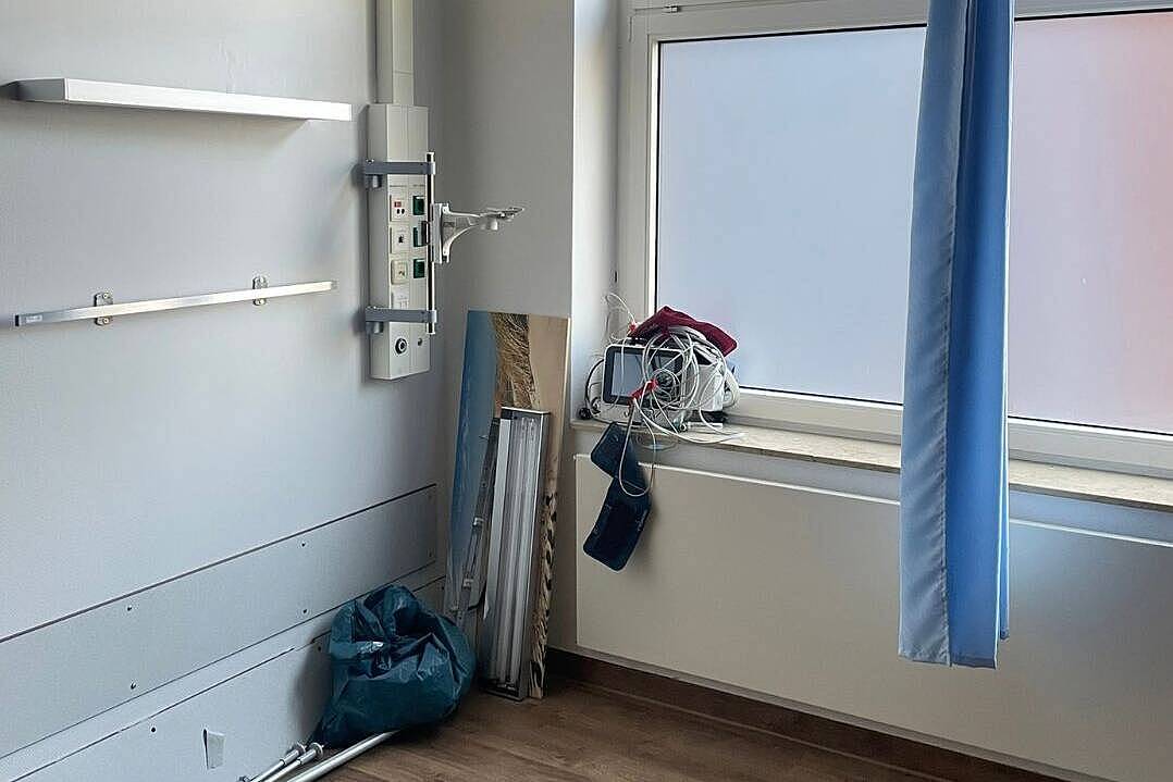 Leeres Patientenzimmer mit Versorgungsleiste, blauem Trennvorhang und abgebauten Geräten auf der Fensterbank