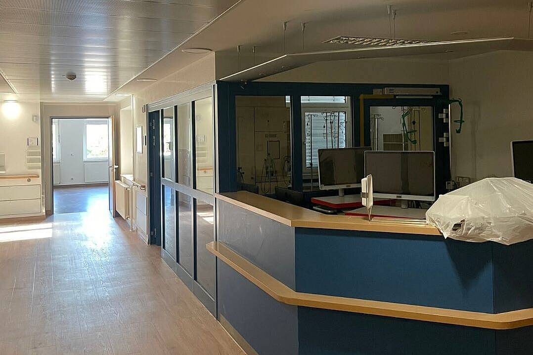 Stationsflur der Station 1b mit blauem Stationstresen, Monitoren und grünem Notausgangsschild, ein Teil des Tresens ist mit Folie abgedeckt