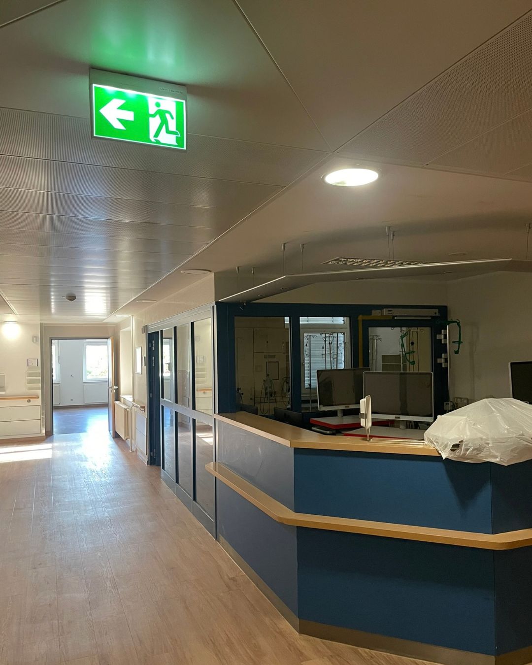 Stationsflur der Station 1b mit blauem Stationstresen, Monitoren und grünem Notausgangsschild, ein Teil des Tresens ist mit Folie abgedeckt