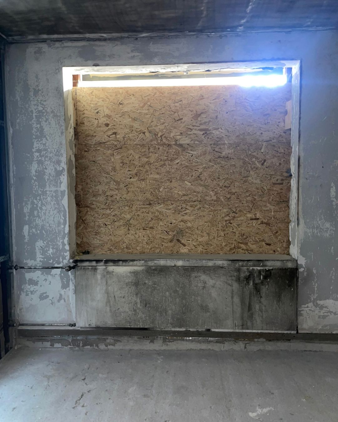 Entkerntes Zimmer mit rußgeschwärzten Betonwänden, das Fenster ist mit einer Holzplatte verschlossen